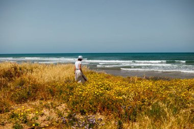 Yaz havası. Beyaz akıcı elbiseli genç bir kadın deniz kıyısında yürüyor. Kız denize bakmaktadır. Kumsalda dinlenmek..