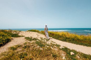 Yaz havası. Beyaz akıcı elbiseli genç bir kadın deniz kıyısında yürüyor. Kız denize bakmaktadır. Kumsalda dinlenmek..