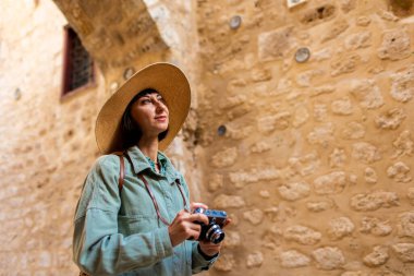 Kameralı kız kamerayı ayarlıyor. Şapkalı, film kamerası olan şık bir kız Arap şehrinin caddesinde duruyor. Film kamerası kapat. Maceralar ve seyahat.