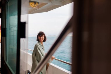 Genç bir kadın bir yolcu gemisinin güvertesinde duruyor ve gülümsüyor. Kız seyahat ederken gülümsüyor. Genç ve güzel bir esmer yat ile seyahat ediyor. seyahat ve macera