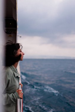 Genç bir kadın bir yolcu gemisinin güvertesinde duruyor ve batan güneşe bakıyor, yakın çekim siluetine. Genç ve güzel bir esmer yat ile seyahat ediyor. seyahat ve macera.