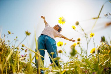 Yaz havası. Mavi gökyüzü ve çiçeklerin arka planında poz veren genç ve neşeli bir adam. Yakışıklı bir adam çiçekler arasında dans eder. Adam dans ediyor. bahar modası.