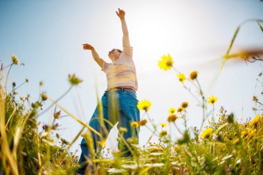 Yaz havası. Mavi gökyüzü ve çiçeklerin arka planında poz veren genç ve neşeli bir adam. Yakışıklı bir adam çiçekler arasında dans eder. Adam dans ediyor. bahar modası.