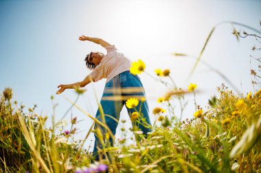 Genç ve neşeli adam çiçekler arasında dans ediyor. Doğada dans eden yakışıklı adam. Yaz havası. Çiçeklerin arasında mutlu bir genç adam, açık havada. bahar modası.