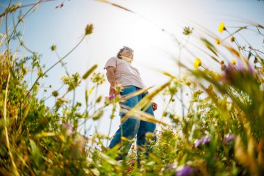Yaz havası. Mavi gökyüzü ve çiçeklerin arka planında poz veren şık giyinmiş genç bir adam. bahar modası.