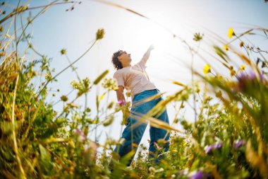 Yaz havası. Genç ve neşeli bir adam mavi gökyüzü ve çiçeklerle dans ediyor. Yakışıklı bir adam çiçekler arasında dans eder. Çiçeklerin arasında mutlu bir genç adam, açık havada. bahar modası.