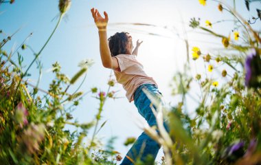 Yaz havası. Mavi gökyüzü ve çiçeklerin arka planında poz veren genç ve neşeli bir adam. Yakışıklı bir adam çiçekler arasında dans eder. Adam dans ediyor. bahar modası.