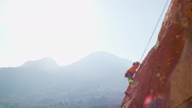 Yaz kampında spor. Bir çocuk yaz kampında kaya tırmanışı yapıyor. Dağcı çocuk. Güneşli bir günde doğada spor. Sevimli genç, kayaya bağlanmış bir şekilde tırmanıyor. Aktif tatil. Yaz tatili.