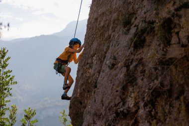 Çocuk kaya tırmanışı. Bir çocuk dağın arka planına karşı bir kayaya tırmanır. Olağanüstü bir hobi. Güçlü olmak için atletik çocuk eğitimi. Yükselen güvenlik.