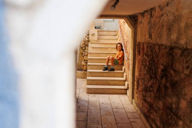 Merdivenlerde oturan bir çocuk mavi duvarlı büyüleyici bir Akdeniz caddesine doğru gidiyor. Akdeniz şehri. Çocuklarla seyahat et.