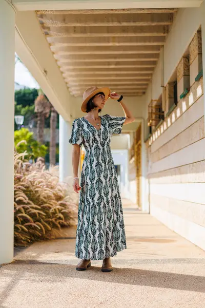 Açık havada, sokakta yürüyen, elbise ve şapka giymiş güzel esmer bir kadının uzun bir portresi. moda ve tarz kavramı.