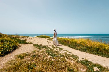 Yaz havası. Kollarını kaldırmış, beyaz elbiseli mutlu genç bir kadın deniz kıyısında yürüyor ve denize bakıyor. Kumsalda dinlenmek..