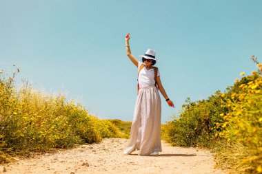 Yürüyüşten zevk alan mutlu bir kadın. Yaz havası. Elbiseli ve sırt çantalı bir kız. Güzel tepelerin ve güzel manzaraların arka planında elbise giymiş genç bir kadının portresi.