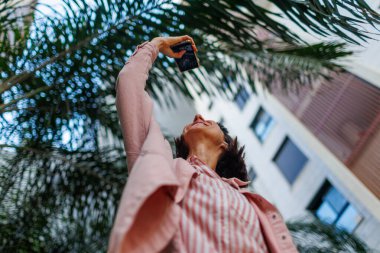 Neşeli aktif kadın güzel bir şehir parkının fotoğrafını çekiyor. Şehir manzarasının fotoğrafını çekmek için modern akıllı telefonu kullanan mutlu bir kız. Çekici turist kız dışarıda fotoğraf çekmeyi seviyor.