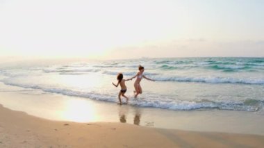 Plajda yaz günü. Mutlu genç bir anne sahilde oğluna sarılıyor, ailesi gülüyor ve birlikte eğleniyor. Çocuğu olan genç bir anne. Aile deniz tatili.