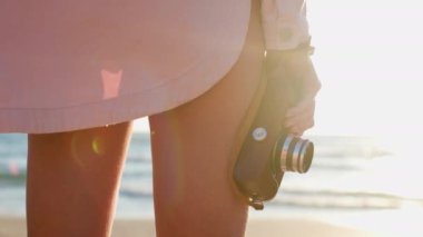 Kameralı kız. Elinde kamera olan bir kadın sahilde duruyor ve tatili boyunca deniz manzarasından zevk alıyor. Arkadan bak. macera tatili