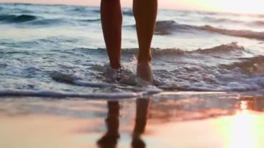 Yaz havası. Arkadan bak. Kadın denizde duruyor. Bacaklarını kapat. Deniz suyu köpüğü gün batımında genç ve güzel bir kızın ayaklarını ve kumları yıkar. Hafta sonu doğa gezisi..