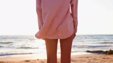 Yaz havası. Sahildeki kız. Arkadan bak. Pembe tişörtlü ince kız kumlu bir sahilde duruyor ve denize bakıyor. Barış ve sevgi. Sağlıklı yaşam tarzı ve seyahat kavramı.