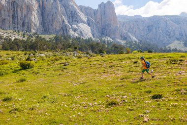 Dağlarda yürüyüş. Sırt çantalı küçük bir çocuk dağların ve bulutların ardında bir patika boyunca yürüyor. Hafta sonu yürüyüş için aktif sağlıklı yaşam tarzı. Seyahat kavramı