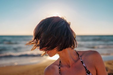 Kumsalda güzel bir esmerin portresi. Genç mutlu kız gülümsüyor. Saç yüzünü kapatır. Rüzgar saçlarınla oynuyor. Yüz kılları. Yaz tropik havası