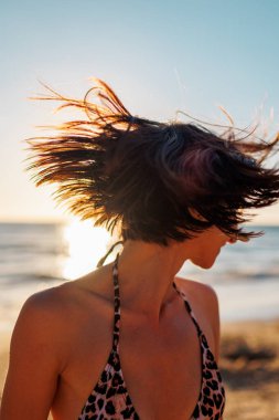 Yaz havası. Kumsalda güzel bir esmerin portresi. Genç mutlu kız gülümsüyor. Saçında rüzgar var. Saç yüzünü kapatır. Genç bir kız sahilde eğleniyor.