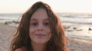 Uzun saçlı ve yüzünde mutlu bir gülümseme olan yakışıklı bir çocuk. Kumsalda mutlu bir çocuk. Uzun saçlı, gülümseyen bir çocuğun yakın plan portresi..