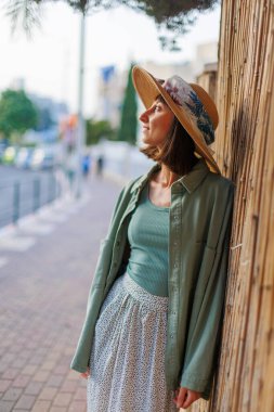 Genç bir esmer şehirde dururken mutlu bir şekilde gülümsüyor. Gömlekli, etekli ve şapkalı şık bir kız avlunun yanında duruyor. Yaz Portresi