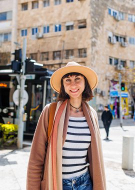 Güneşli bir havada şehrin arka planına karşı şapkalı neşeli beyaz bir kadının portresi. İlginç yerlere seyahat et. Kameraya gülümseyen şapkalı şık bir kızın fotoğrafı..