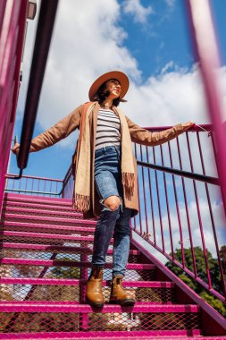 Şapkalı şık bir kız. Kendine güvenen bir kız merdivenlerden çıkar. Genç kız şehirde yürüyüş yapıyor. Moda tarzı.