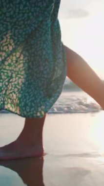 Dikey çekim. Kadın bacakları yakın plan. Elbiseli bir kadın kumsalda yürüyor. Elbiseli bir kız kumda yürüyor. Sahilde gün batımı.