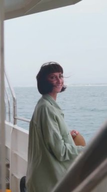 Dikey çekim. Genç bayan bir yolcu gemisinin güvertesinde duruyor ve yolculuğun tadını çıkarıyor. Mutlu kadın. Yatta, tatilde ve seyahatte olan bir kadın. seyahat ve macera.