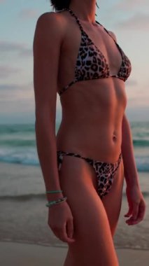 Dikey çekim. Sahilde yürüyüşün tadını çıkarıyorum. Mayo giymiş ince bir kadın gün batımında sahilde yürüyor. Gün batımında bir kız sahilde yalınayak yürüyor..