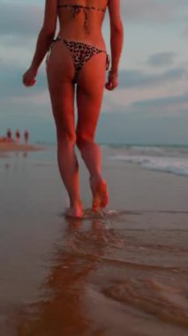 Dikey çekim. Sahilde yürüyüşün tadını çıkarıyorum. Gün batımında kumsalda mayo giymiş ince bir kız koşuyor..