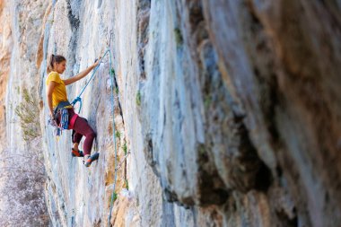  Kız kayaya tırmanıyor. Dağcı kız. Bir olimpiyat sporu olarak kaya tırmanışı. Bir kadın doğada spor yapar.