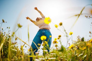 Yaz havası. Genç ve neşeli bir adam mavi gökyüzü ve çiçeklerle dans ediyor. Yakışıklı bir adam çiçekler arasında dans eder. Çiçeklerin arasında mutlu bir genç adam, açık havada. bahar modası.