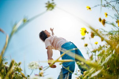 Yaz havası. Mavi gökyüzü ve çiçeklerin arka planında poz veren genç ve neşeli bir adam. Yakışıklı bir adam çiçekler arasında dans eder. Adam dans ediyor. bahar modası.