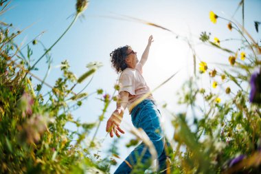 Yaz havası. Genç ve neşeli bir adam mavi gökyüzü ve çiçeklerle dans ediyor. Yakışıklı bir adam çiçekler arasında dans eder. Çiçeklerin arasında mutlu bir genç adam, açık havada. bahar modası.