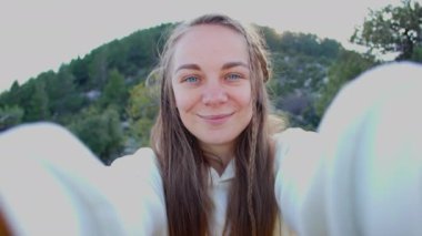 Sarı saçlı genç bir kadın dağlarda yürüyüş yaparken selfie çekiyordu. Uçurumun tepesinde kameraya gülümseyen mutlu bir yürüyüşçü. Seyahat ve hobi konsepti.