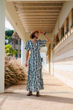 Elbiseli ve şapkalı genç kız caddede yürüyor. Sokakta yürü, güneşli hava, hafta sonu.