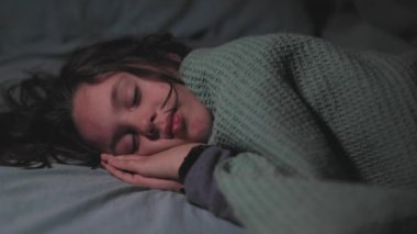 Çocuk yatakta huzur içinde uyuyor, kıvrılıp gözlerini kapatıyor. Oda loş bir şekilde aydınlandı ve o bir battaniyeyle kaplandı..