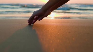 Romantik ruh hali. Kızlar ıslak sahil kumuna elleriyle çizerler. Aşk ve tutku kavramı. Sahilde gün batımı.