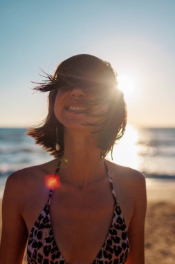 Sahilde gün batımında seksi bir mayo giymiş güzel esmer bir kadının yakın plan portresi. Yüz kılları. Yaz tropik havası.