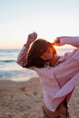 Yaz havası. Sahildeki kız. Pembe gömlekli ve mayolu mutlu genç kız sahilde dinleniyor. Mutlu kadın. Kız kumsalda duruyor. Kumsalda dinlenmek.