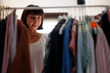 Evde gardırop ya da giyim mağazasının soyunma odası. Genç bir kadın evdeki ya da mağazadaki dolabından şık bir kıyafet seçer. Kız ne giyeceğini düşünüyor..