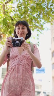 Dikey çekim. Genç bir bayan gezgin şehirde analog bir kamera kullanarak fotoğraf çekiyor. Kameralı kadın fotoğrafçı dışarıda fotoğraf çekiyor.