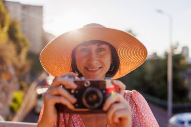 Şapkalı genç kız. Yaz havası. Kameralı kadın fotoğrafçı dışarıda fotoğraf çekiyor. Fotoğrafçı objektife nişan alır ve çekim işleminden zevk alır. seyahat ve tatil.