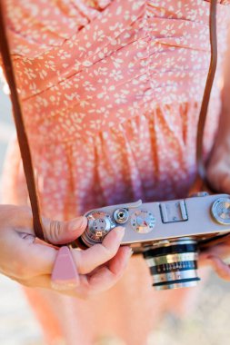 Kameralı genç bir kız. Fotoğrafçı kamerayı ayarlar. Elinde analog film kamerası olan modaya uygun bir kadın. seyahat ve tatil.