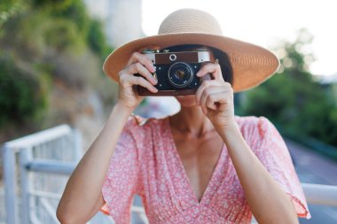 Pembe elbiseli ve şapkalı genç bir kadın şehirde kameraya çekiliyor. Analog bir kamerayla fotoğraf çekiyor. seyahat ve tatil.