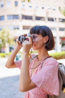 Genç bir gezgin, analog kamera kullanarak şehrin fotoğraflarını çekiyor. Kameralı kadın fotoğrafçı dışarıda fotoğraf çekiyor. Kadın, turist, şehir manzarası..