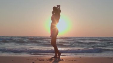 Sahilde dans eden kız. Çekici, mutlu, elbiseli ve şapkalı genç bir kadın gün batımında boş vakitlerin tadını çıkarıyor. Bahar yaşam tarzı kavramı, özgürlük.